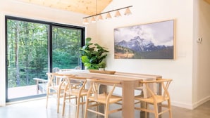 A dining area with a wooden table and chairs, a potted plant, and a large window with a view of trees. - NEW-Casa Vetta 4BR Davis Cabin, Deck, Fire Pit (Davis)