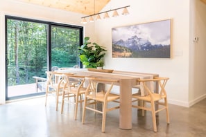 Un comedor con una mesa y sillas de madera, una planta en maceta y un ventanal con vistas a árboles.