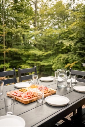 Una mesa de comedor al aire libre, preparada con platos, vasos y diversos alimentos.