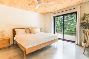 Un dormitorio con techo de madera, una cama grande, una mesita de noche, una planta en maceta y vistas al exterior.