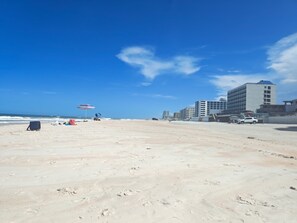 A beach with footprints, a striped umbrella, and buildings in the background. - Complex With Lots of Amenities and Across the street from Beach (Daytona Beach)