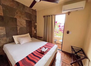 A bedroom with a bed, a window with curtains, an air conditioning unit, and a small table. - Downtown apartment located 3 blocks from the beach and 5th Avenue (Playa del Carmen)