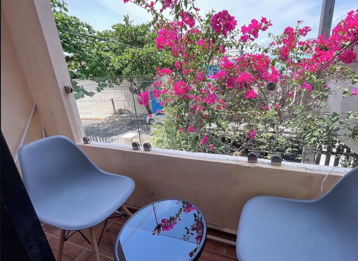 Un balcon avec deux chaises et une petite table, donnant sur un jardin où poussent des fleurs roses.