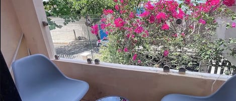 Een balkon met twee stoelen en een kleintje tafeltje, met uitzicht op een tuin vol roze bloemen.