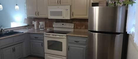 Una cocina con gabinetes blancos, un refrigerador de acero inoxidable, un microondas, una estufa y una cafetera.