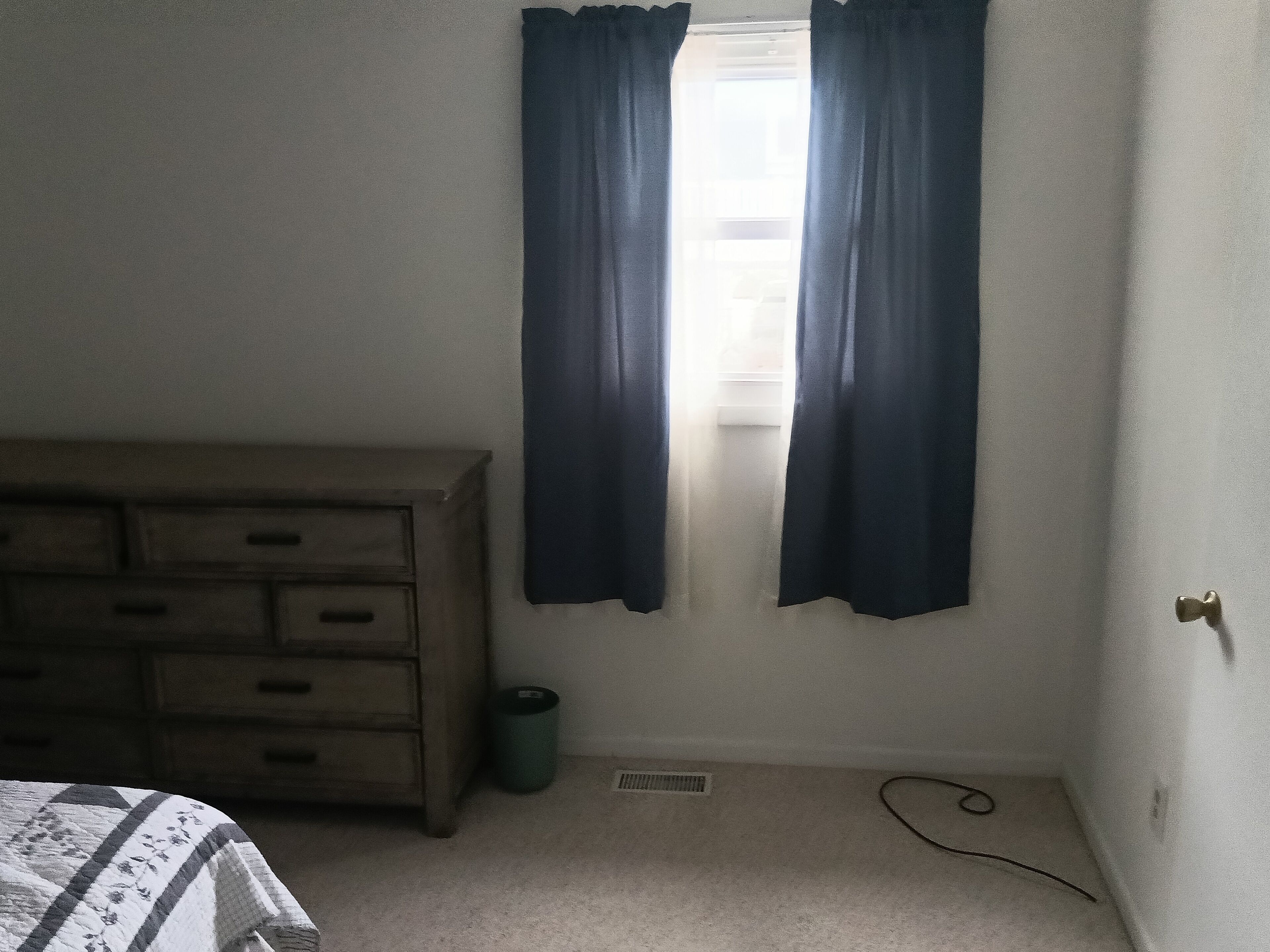 Ein Schlafzimmer mit einem Holzkasten, einem Heizkörper und einem Fenster mit Vorhängen.