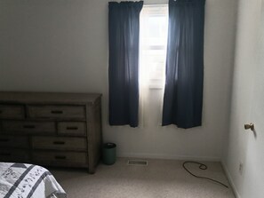 Una camera da letto con un comò in legno, un termosifone e una finestra con tende.