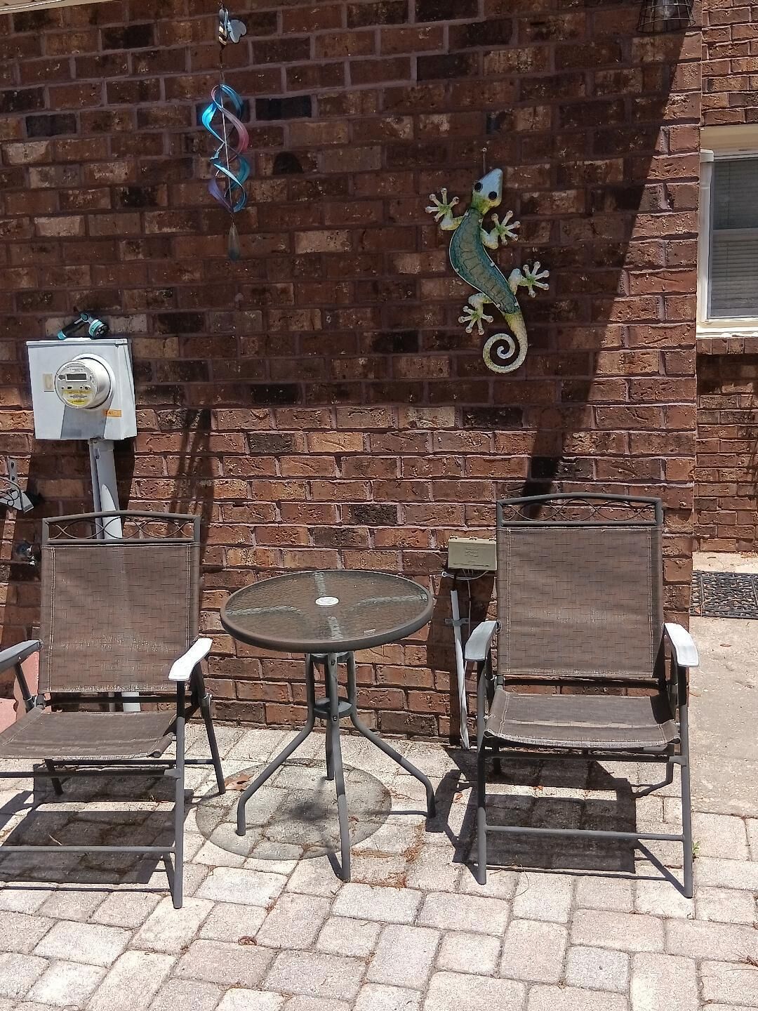 A brick wall with a decorative gecko, a round table, and two chairs.