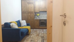 Ein Zimmer mit einem blauen Sofa, einem Holzschrank und einer Küchenzeile mit einem Herd.