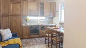 A compact kitchen with wooden cabinets, a built-in oven, and a dining area with a table and chairs. - Casa della Marmotta by Ca-sa Check (Aprica)