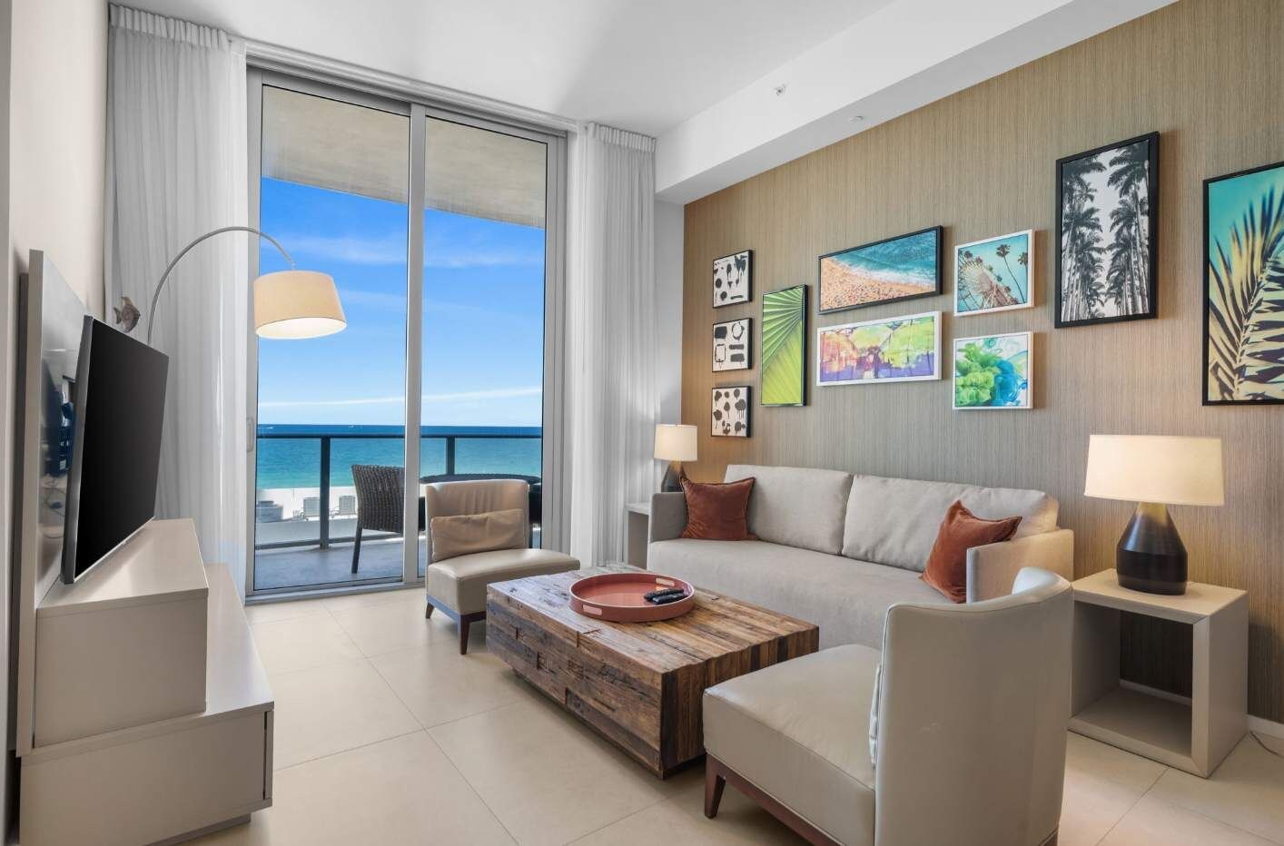 Een moderne hotelkamer met een ruim balkon, een flatscreen televisie, een bank, een salontafel en kunstwerken aan de wanden.