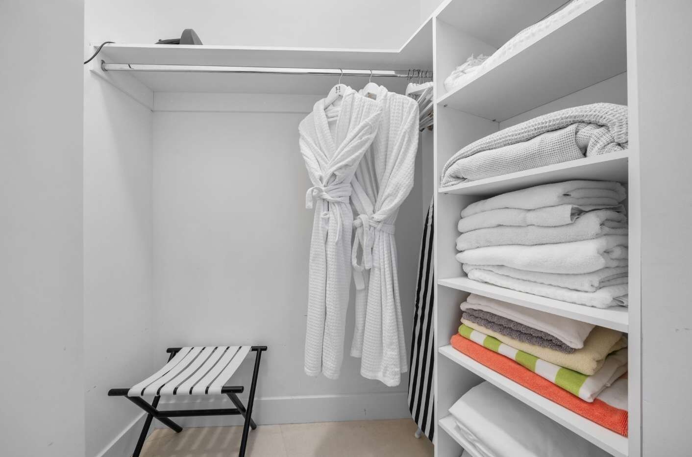 Un dressing avec un portant pour les peignoirs, des étagères pour les serviettes pliées et un petit banc.