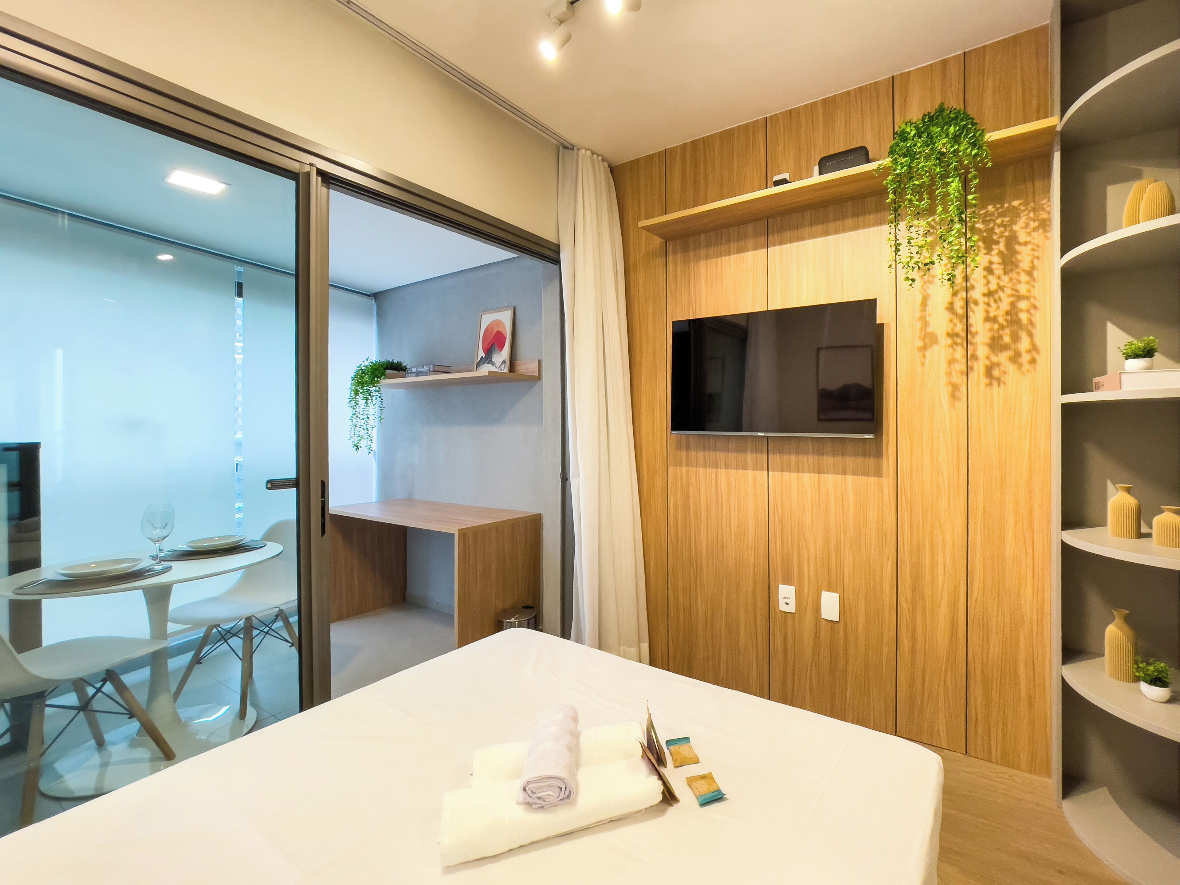 Ein modernes Hotelzimmer mit Bett, Fernseher, Holzverkleidung, einem kleinen Schreibtisch und einer Glastrennwand.