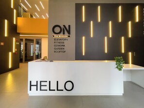 Ein Empfangstresen mit einem 'HELLO'-Schild, eine Wand mit 'ON' und Serviceoptionen sowie moderne Beleuchtung.