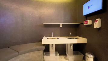 A modern bathroom with a white sink, a mirror, a towel rack, and a television mounted on the wall.