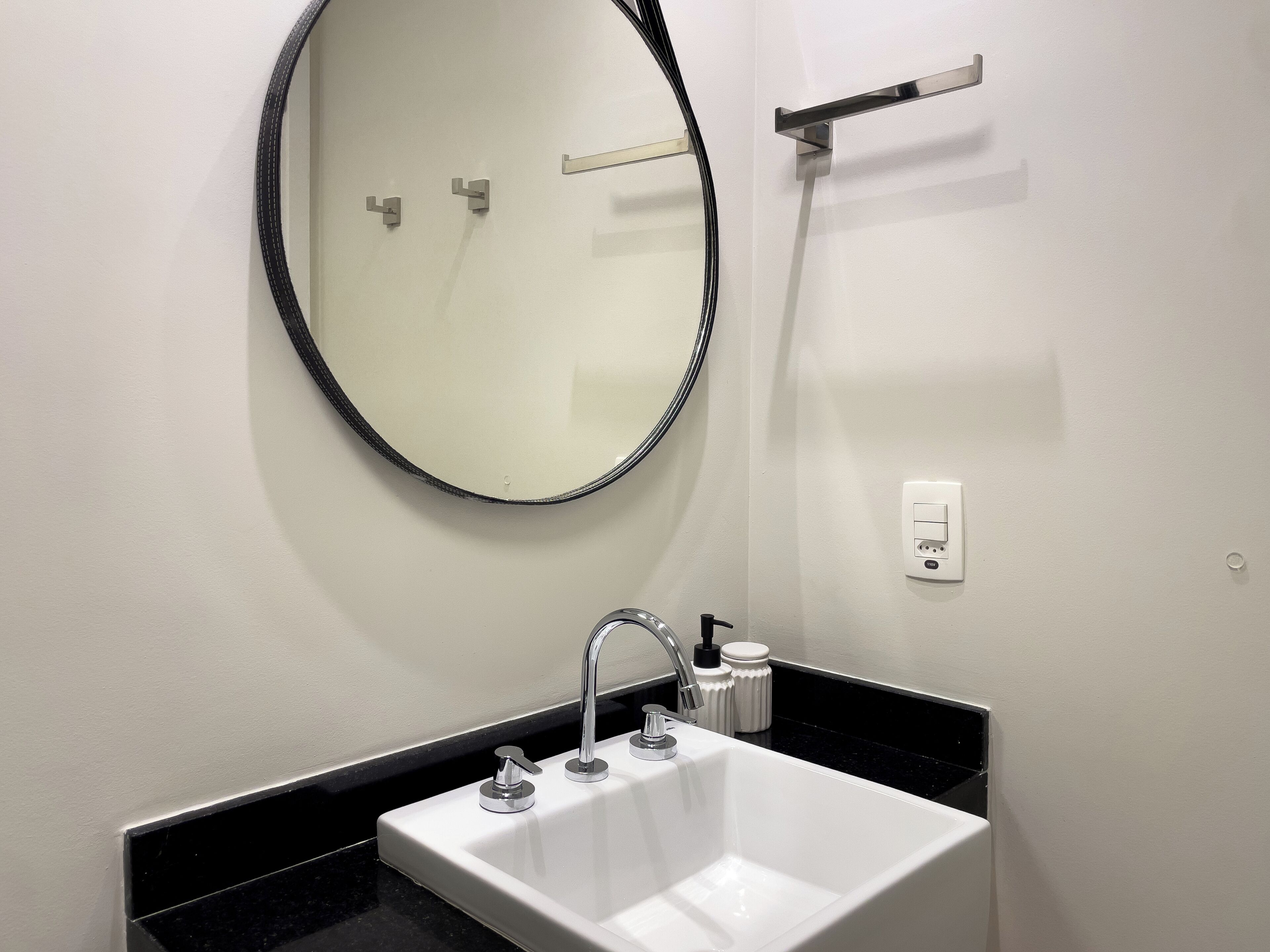 A bathroom with a white sink, chrome faucet, and a round mirror.
