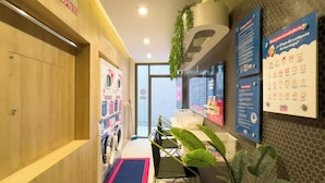 Un vestíbulo de hotel con una recepción, un panel informativo en la pared y una planta.