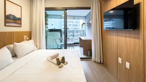 Habitación de hotel con cama, televisor montado en la pared, balcón con mesa y sillas, y un cuadro en la pared.