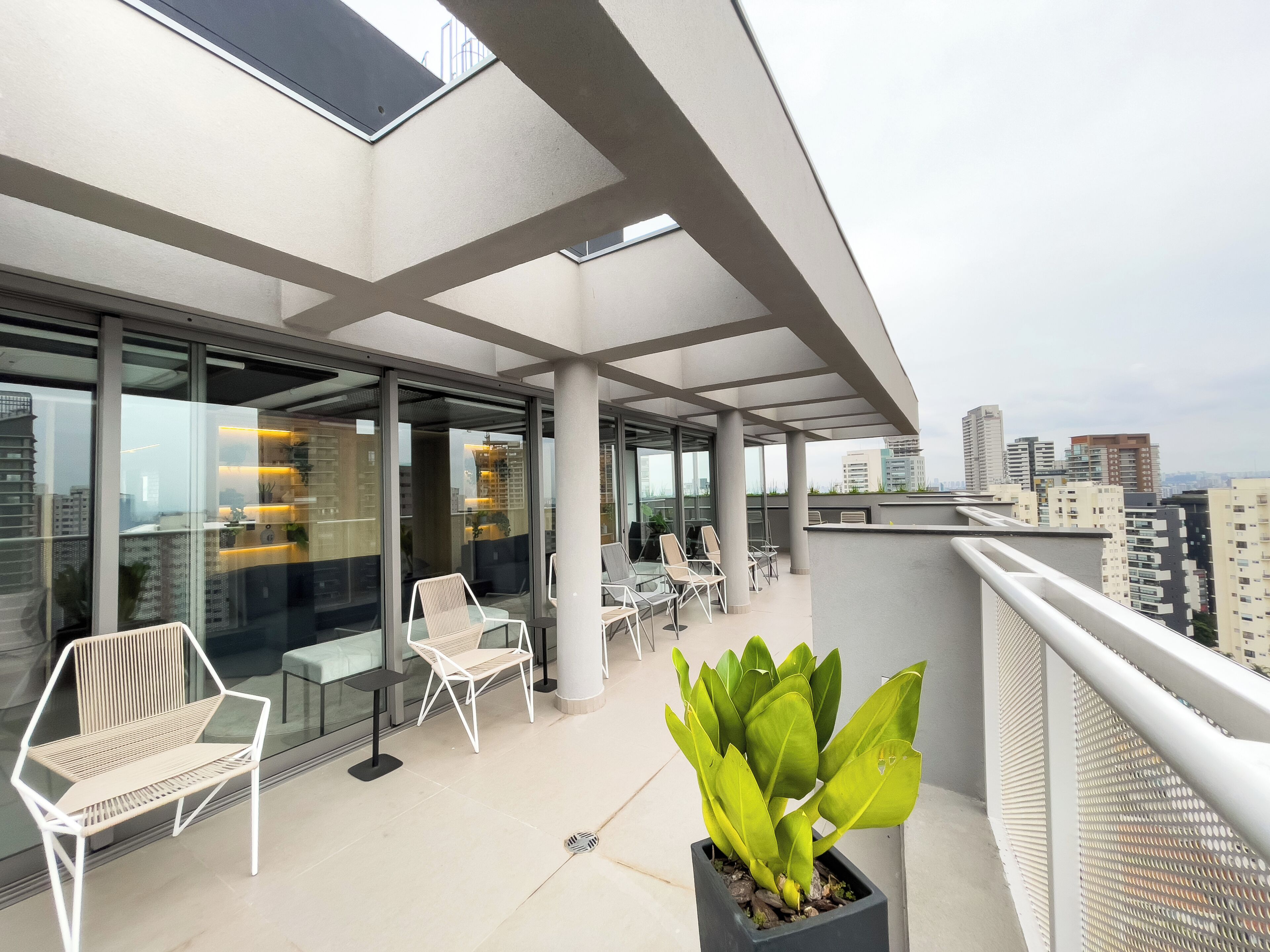 Un balcón exterior con asientos, una planta en maceta y vista a la ciudad.