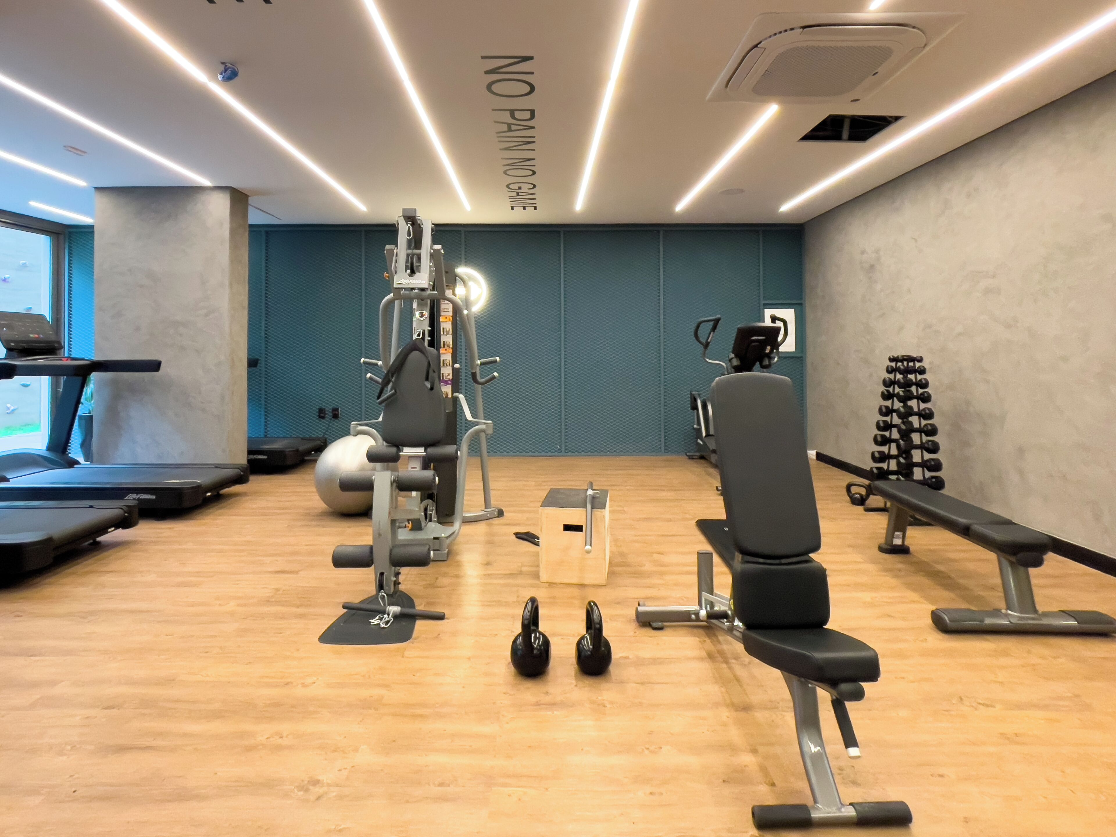 Ein Fitnessraum mit Laufbändern, einer Hantelbank, Kettlebells und einem an der Wand befestigten Trainingsgerät.