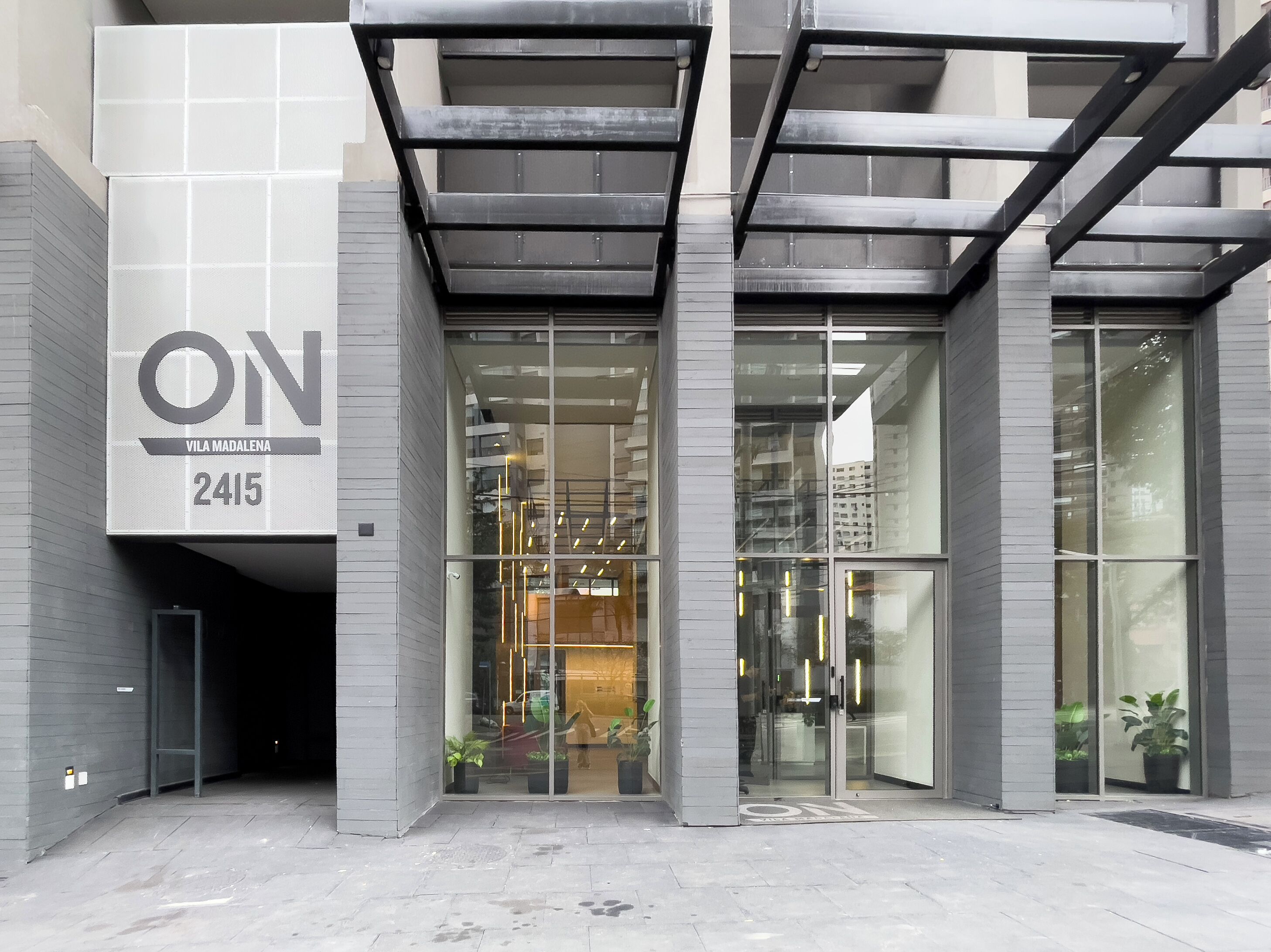 Entrada moderna de un edificio con un gran letrero que dice 'ON VILA MADALENA 2415'.