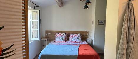A bedroom with a bed, a nightstand, a lamp, and a window.