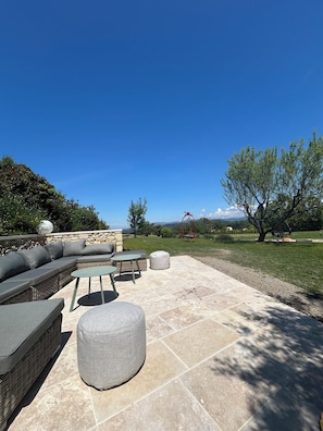 An outdoor patio with a sectional sofa, ottomans, and a stone wall.