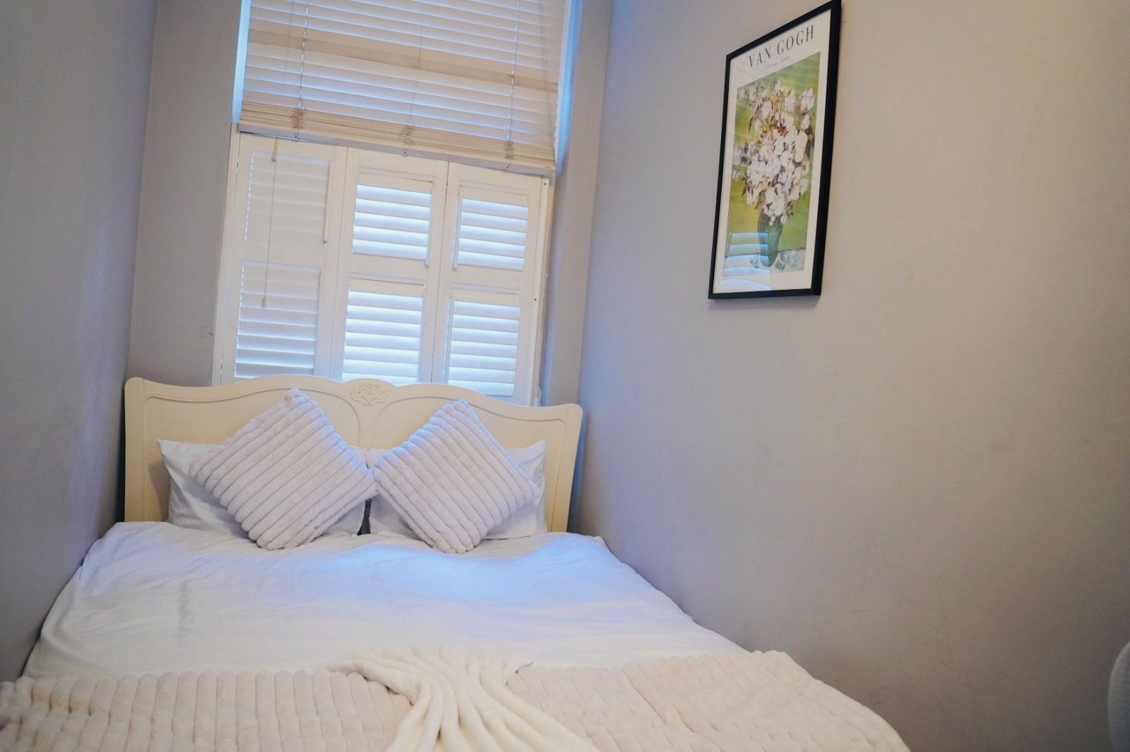 Une chambre à coucher avec un lit, des oreillers, une fenêtre avec des stores et un tableau encadré au mur.