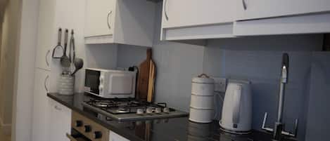 Una cocina con armarios blancos, estufa a gas, microondas, hervidor y bloque de cuchillos.