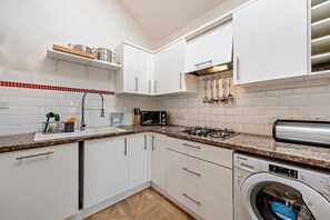 A modern kitchen with white cabinets, a granite countertop, a built-in microwave, a gas stove, and a front-loading washing machine. - Host & Stay | Thornbank (Chichester)