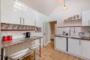 A modern kitchen with white cabinets, a granite countertop, a coffee machine, and a bar stool. - Host & Stay | Thornbank (Chichester)