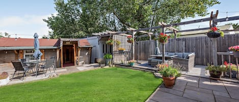 En trädgård med en uteplats, ett område för grillning och en hängande blomkorg.