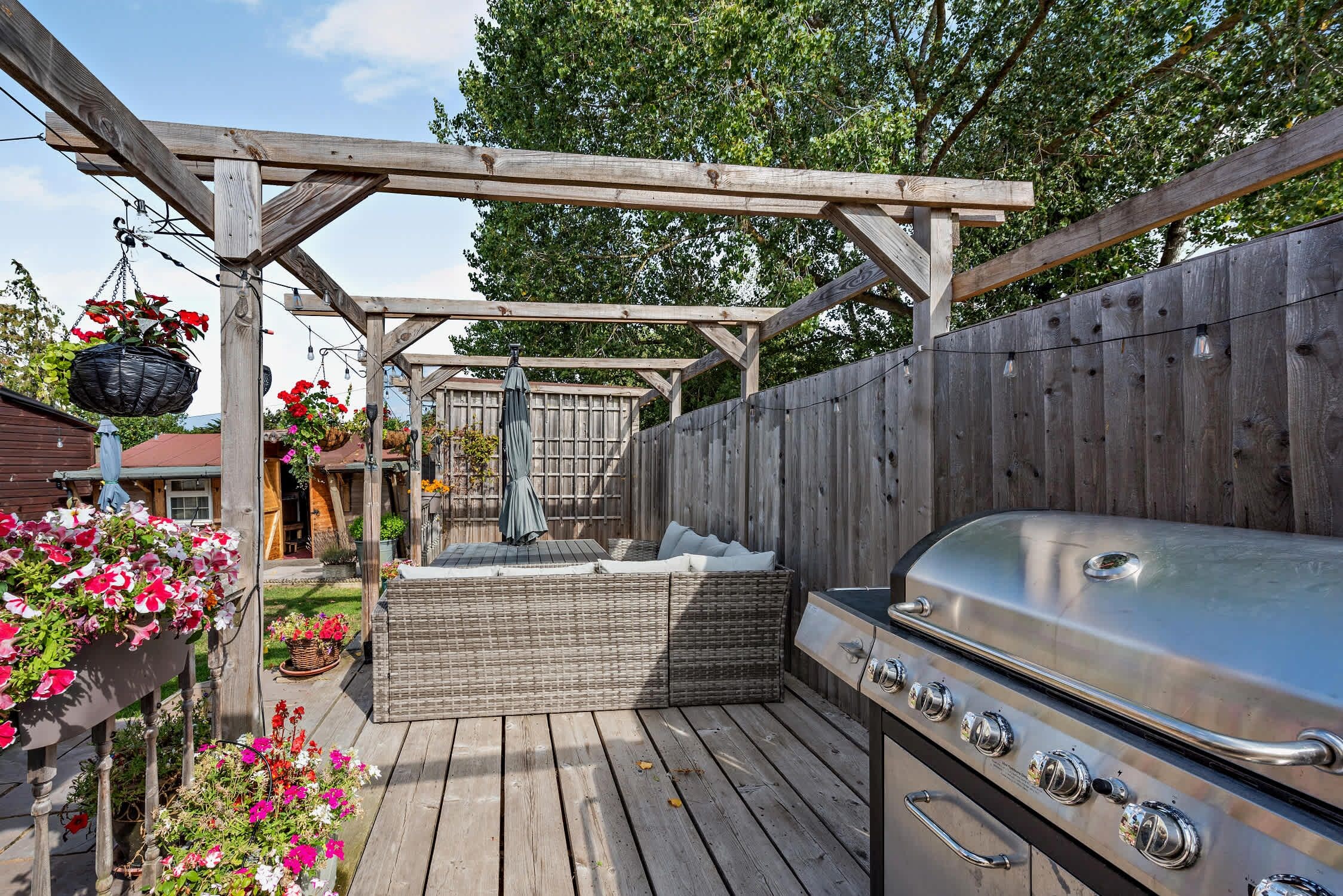 A wooden deck with a barbecue grill, a hot tub, and hanging flower baskets.