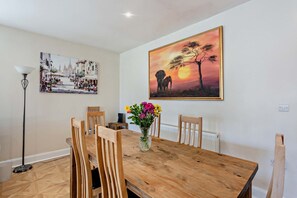 A dining area with a wooden table, chairs, a vase of flowers, and two paintings on the wall. - Host & Stay | Thornbank (Chichester)