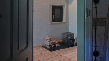 Ein Zimmer mit Holzboden, Deckenbalken und einer Wandleuchte sowie einem kleinen Fenster.