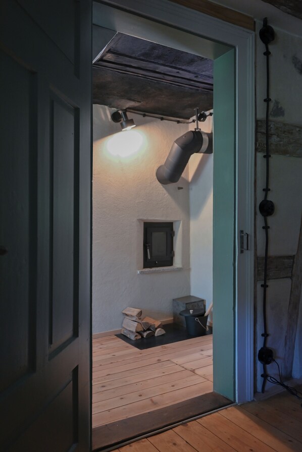 A room with a wooden floor, a ceiling with exposed beams, a wall-mounted light fixture, and a small window.