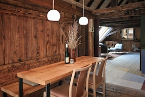 A wooden dining table with chairs, a bottle, and a vase with branches.