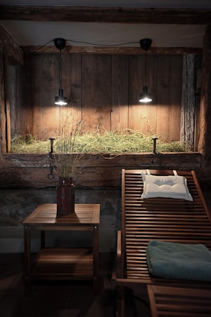 A rustic room with a wooden bench, a small table with a vase, and a window with a view of grass.