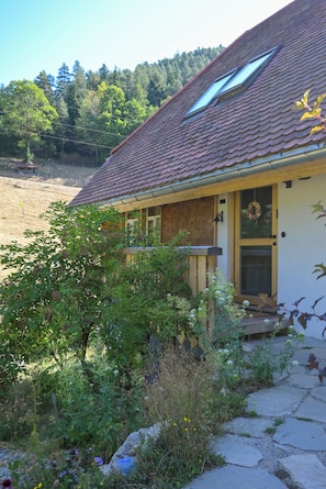 A house with a sloped roof, a front porch, and a garden area with various plants and flowers.