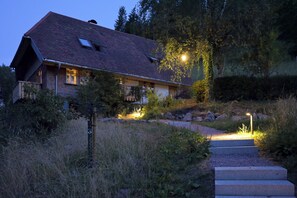 Una casa amb teulada inclinada, una xemeneia visible i un camí cap a l'entrada.