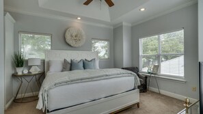 A bedroom with a large bed, a round wall decoration, a desk with a lamp, and a window with blinds. - Golf Cart+4 Bikes | Ventana to the Gulf (Santa Rosa Beach)