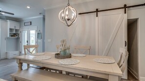 A dining area with a large table, chairs, a chandelier, and a sliding barn door. - Golf Cart+4 Bikes | Ventana to the Gulf (Santa Rosa Beach)