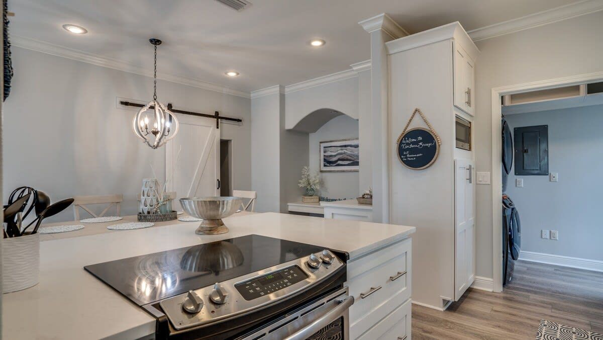 Una cocina moderna con una isla central, horno empotrado y muebles de color blanco.