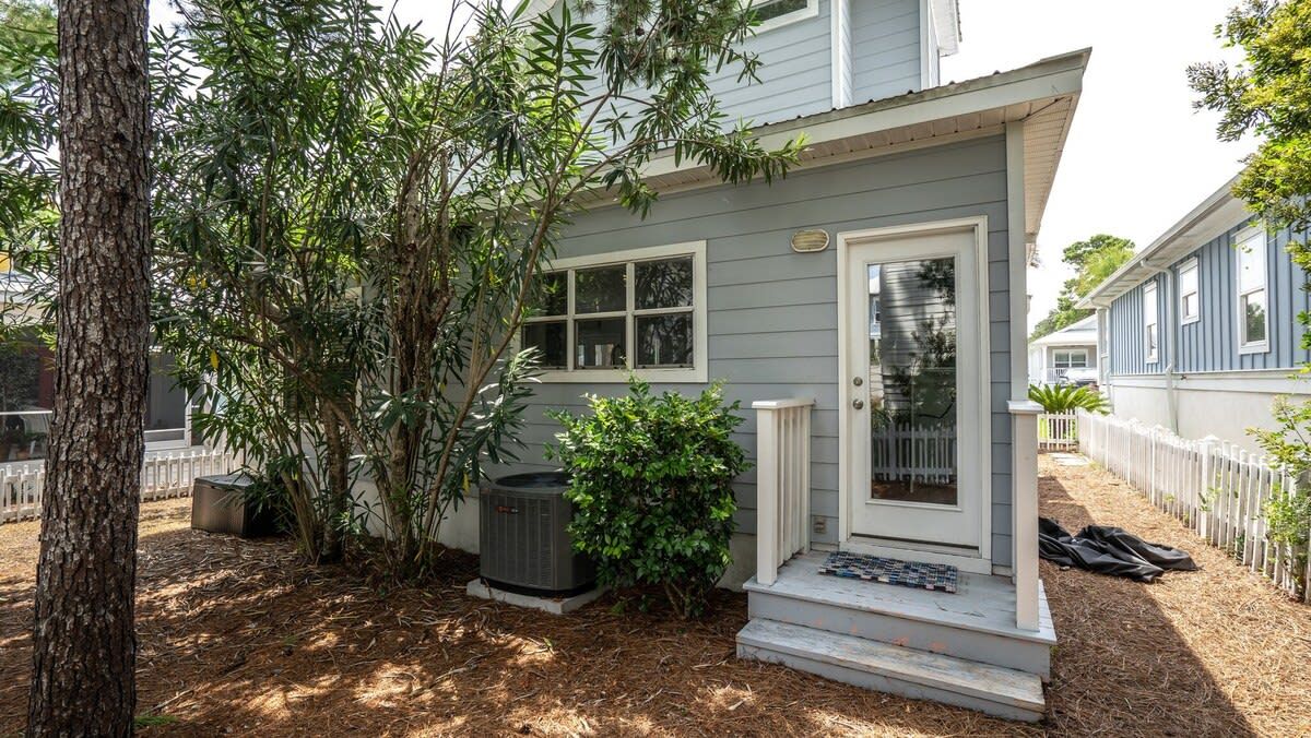 A residential house with a front porch, a small tree, and a white fence.