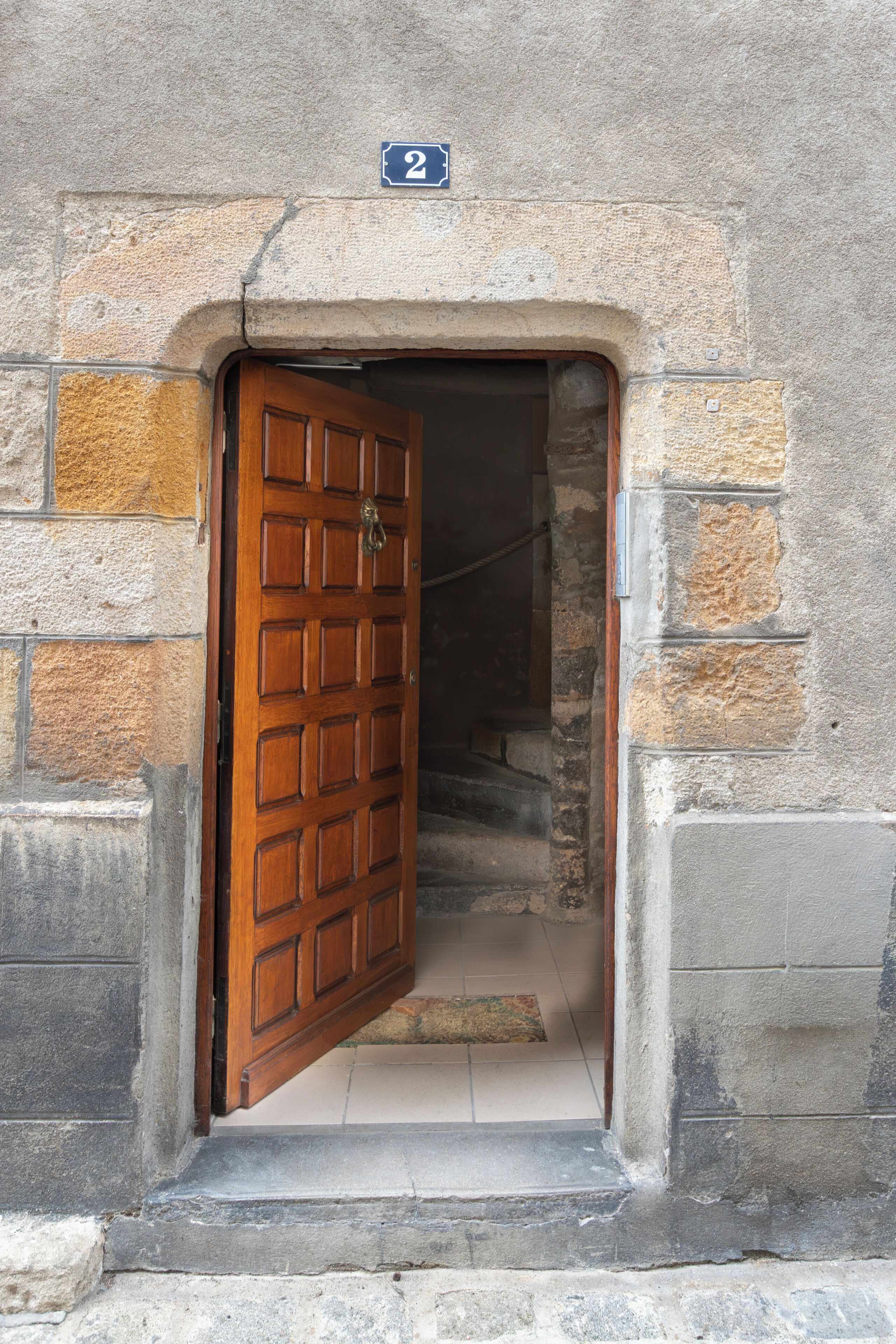 A wooden door with a brass knocker, set in a stone wall with a number plate above indicating the location.
