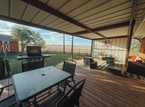 Un patio exterior techado con una mesa, sillas, una parrilla y una zona de estar con cojines.