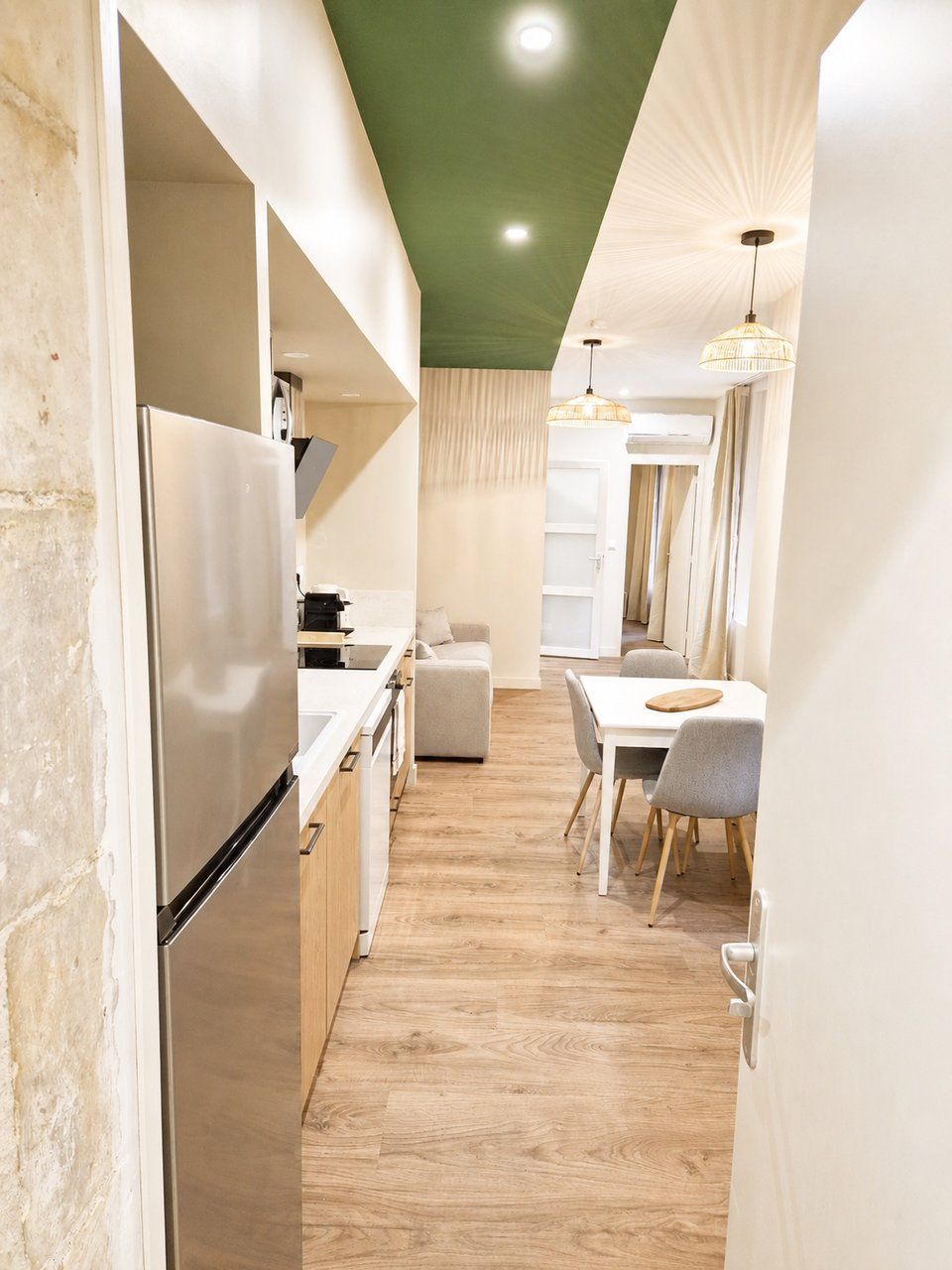 A modern kitchen with a built-in refrigerator, wooden flooring, and a dining area with a table and chairs.