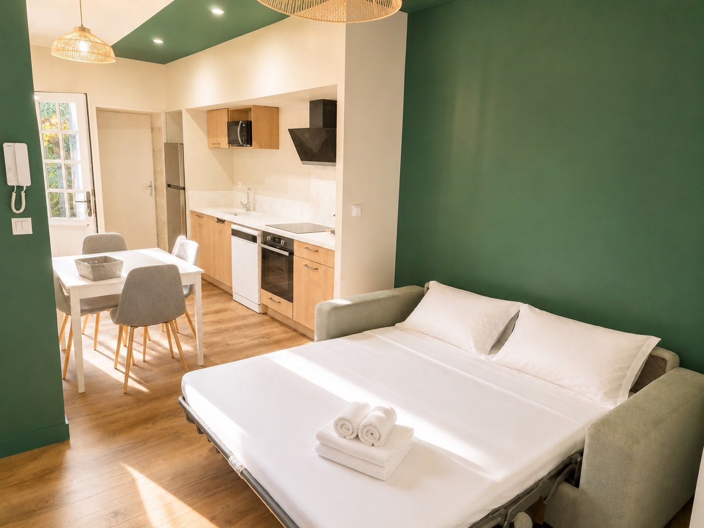 A hotel room with a bed, a small kitchenette, a dining area, and a bathroom.