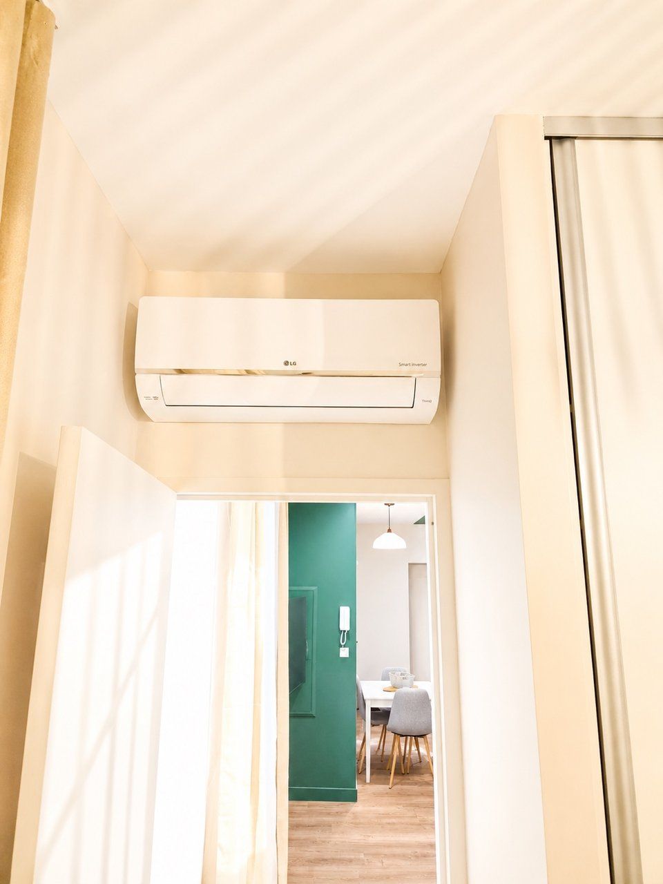 Een hal met een plafondairconditioner, een groene deur naar een eetgedeelte, en een witte muur.