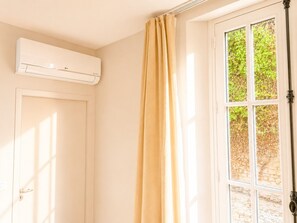 A room with a white door, beige curtains, and a window with a view of greenery.
